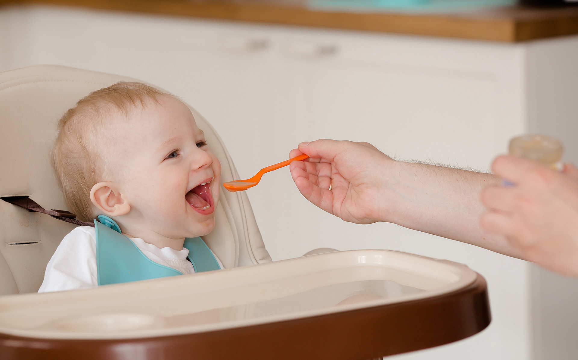 Мама годує дитину, яка сидить в автокріслі, з ложечки